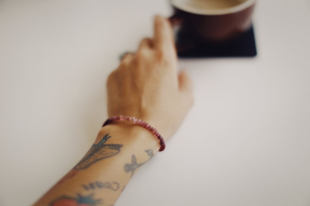 a thulite bracelet on a wrist next to a cup of coffee on a wooden table