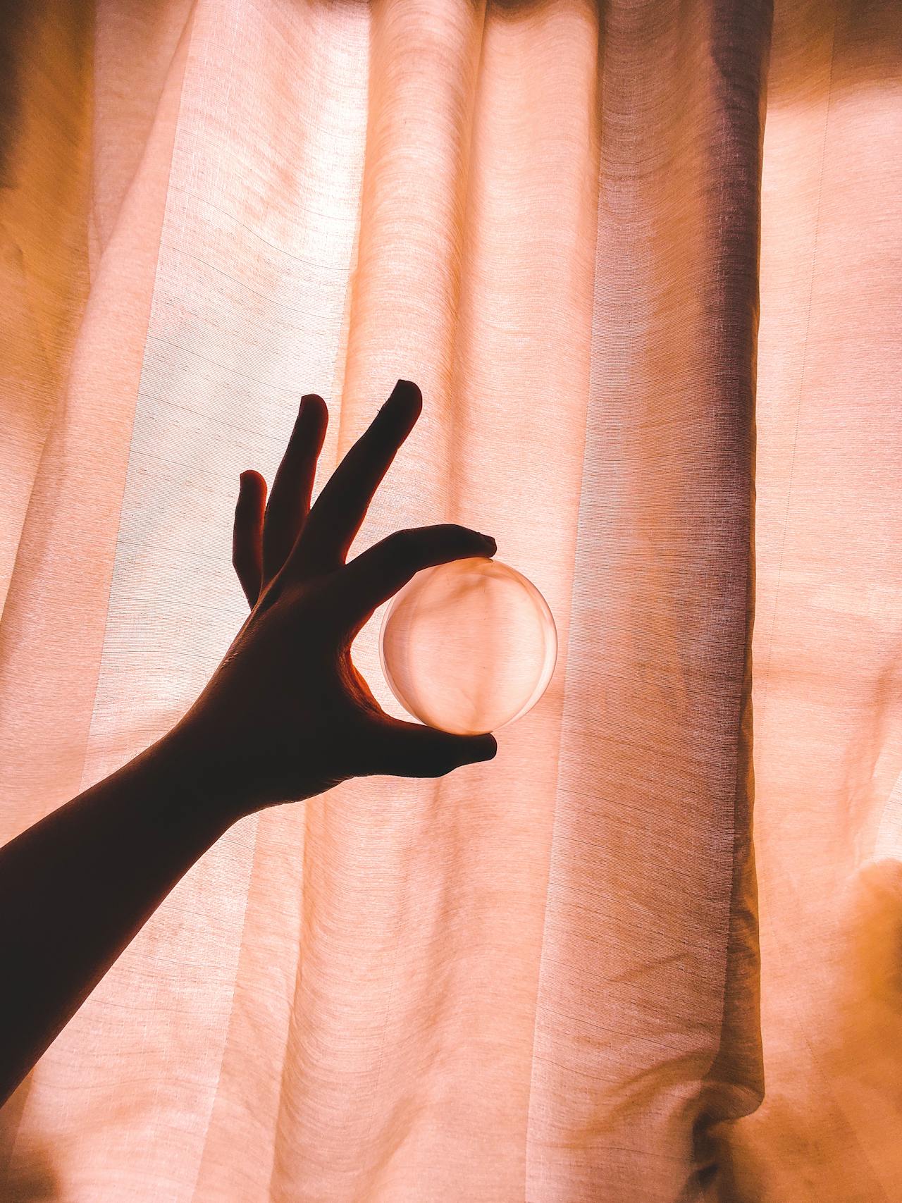 a hand holding a piece of angel aura quartz up to a window with natural light streaming through, showing the color shifts