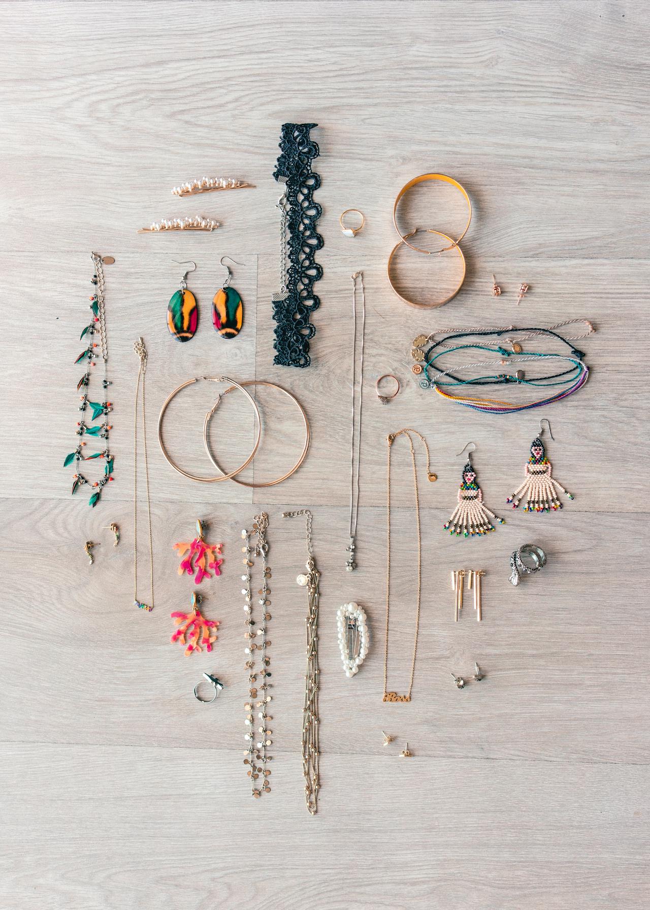 a small collection of jewelry laid out on a bed next to an open suitcase, showing necklaces, rings, and earrings before packing