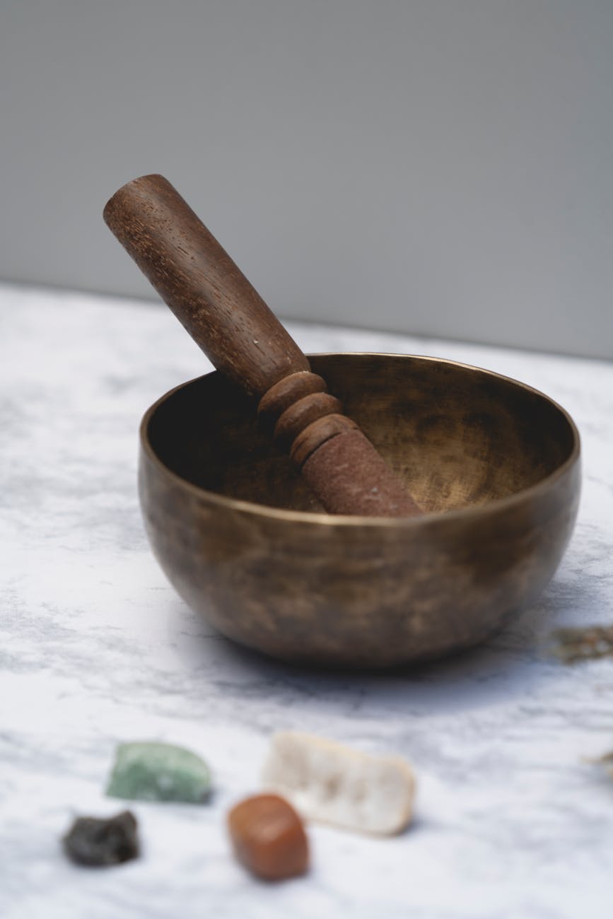 a brass singing bowl on a cushion with a wooden mallet resting beside it, soft natural lighting from a window